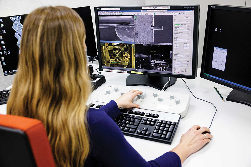A woman sitting in front of a computer and examining a microchip on the screen.