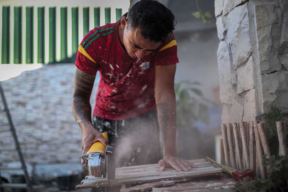 A man in a sports jersey using a circular saw to cut wood.